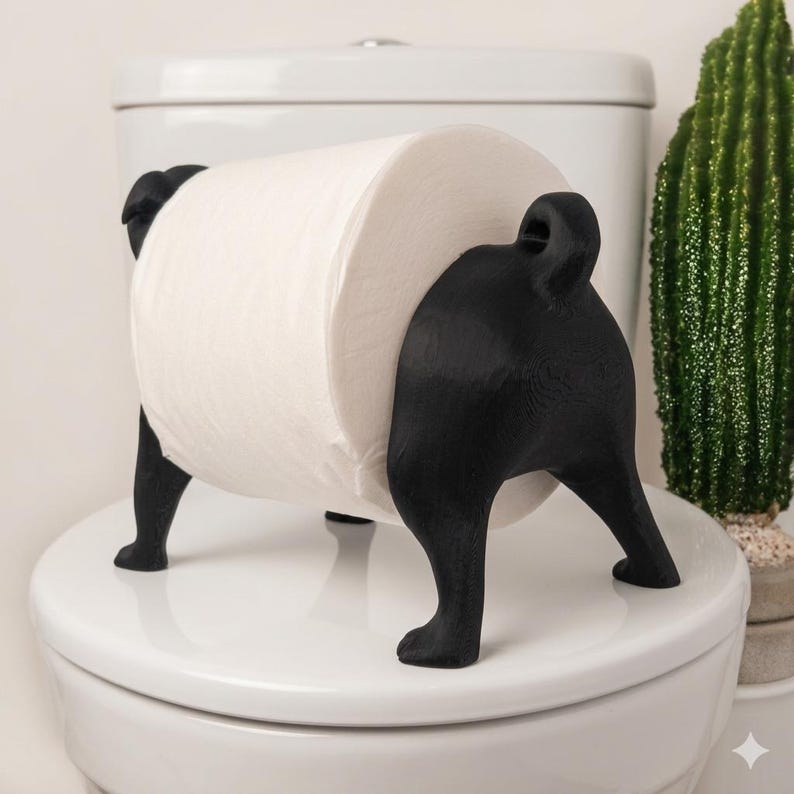 May include: A black, dog-shaped toilet paper holder featuring a stylized canine body with four legs and a curled tail. The holder is designed to support a standard roll of white toilet paper between its front and back sections, creating a functional display.