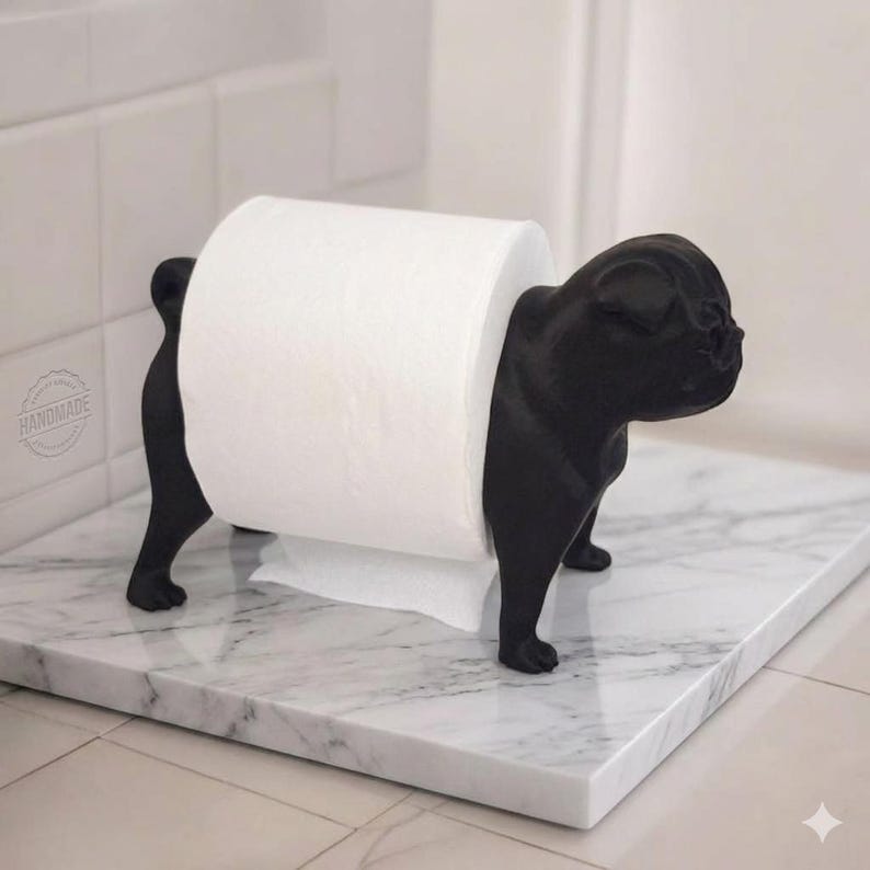 May include: A matte black toilet paper holder shaped like a dog with a stout body and a curled tail. The holder features a white roll of toilet paper positioned between the front and back legs of the dog figure, creating a functional bathroom accessory.