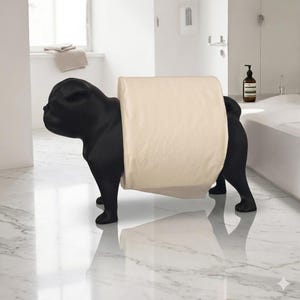 May include: A matte black toilet paper holder shaped like a standing pug dog. The figure features a smooth, solid black finish and holds a single roll of cream-colored toilet paper around its midsection, positioned between its front and back legs.