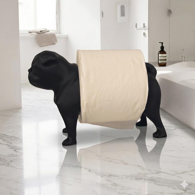 May include: A matte black toilet paper holder shaped like a standing pug dog. The figure features a smooth, solid black finish and holds a single roll of cream-colored toilet paper around its midsection, positioned between its front and back legs.