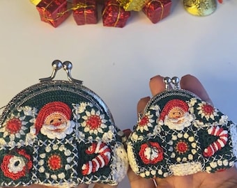May include: Two crocheted coin purses with silver metal clasps. The purses feature a dark green background with white, red, and cream-colored Christmas-themed designs, including Santa Claus faces and candy canes. The purses are held in hands.