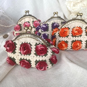May include: Four crochet coin purses with metal clasps. Each purse features a cream-colored base with colorful floral designs. One purse has red roses, another has pink roses, a third has purple roses, and the last has orange roses.