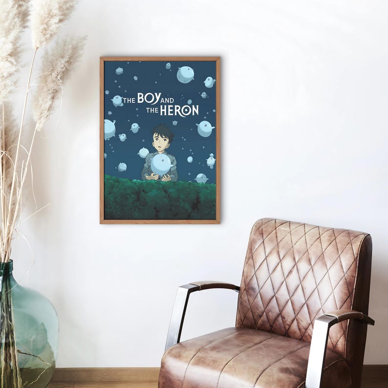 Op de afbeelding: Een poster met een blauwe achtergrond waarop een jonge jongen een gloeiende bol vasthoudt. De poster heeft de tekst "THE BOY AND THE HERON" in wit.