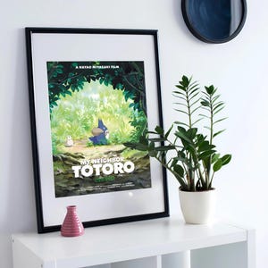 Op de afbeelding: Een zwart ingelijste poster met een groene en blauwe illustratie van een personage uit de film "Mijn buurman Totoro." De poster heeft de titel "Mijn buurman Totoro" in witte tekst op een groene achtergrond.