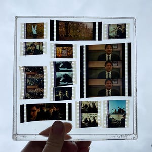 May include: A clear square frame filled with film strips from a movie. The film strips show scenes from a movie with actors and a classroom setting. The film strips are arranged in a grid pattern.