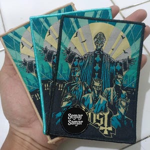 Könnte beinhalten: Drei rechteckige Aufnäher mit einem türkis-schwarzen Design, das eine Figur mit ausgestreckten Armen und andere Figuren darunter zeigt. Die Aufnäher haben einen schwarzen Rand und den Text "Semar Samar" in einem Kreis.