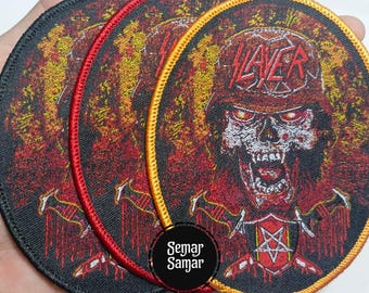 May include: Three round embroidered patches with a heavy metal theme. The patches feature a skull wearing a helmet with the word "SLAYER" and a red and yellow colour scheme. The patches have a black, red, and yellow border.
