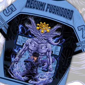 May include: Light blue t-shirt featuring a graphic of a character with the text "MEGUMI FUSHIGORO". The design includes a large purple figure with a golden crown and a smaller figure in black. The number 5 and 7 are on the sleeves.