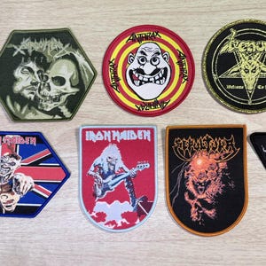 Puede incluir: Una colección de siete parches de tela bordados con varios logotipos de bandas de heavy metal e ilustraciones gráficas, incluyendo Anthrax, Iron Maiden, Sepultura y Venom, con formas diversas como hexágonos, círculos y triángulos.