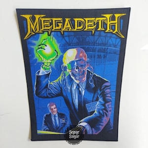 May include: A rectangular fabric patch featuring the yellow Megadeth logo at the top. The graphic depicts a skeletal figure in a suit and sunglasses holding a glowing green orb, with a man in a suit visible in the lower left corner against a blue background.