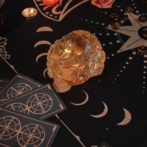 May include: A black cloth with a gold star and moon design. There are tarot cards with gold accents, a clear crystal, and a small candle on the cloth.