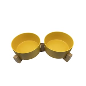 May include: A double pet bowl set with a bright yellow interior and exterior. The bowls are mounted on a natural wood base. The bowls are designed for food or water for pets.