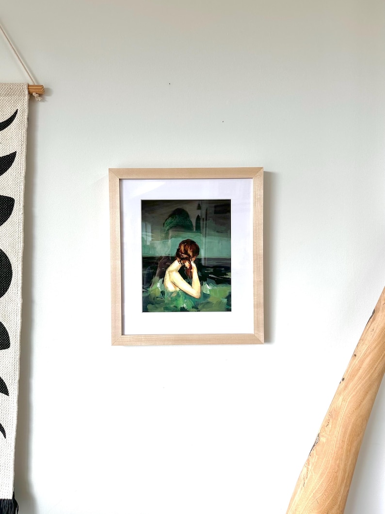 a framed painting of a woman with a pensive expression, hanging on a white wall.