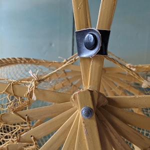 May include: Close-up of a vintage parasol's frame. The frame is made of light-colored wood, with a black leather strap and a metal button. The parasol's netting is visible, and the overall design is intricate and delicate.