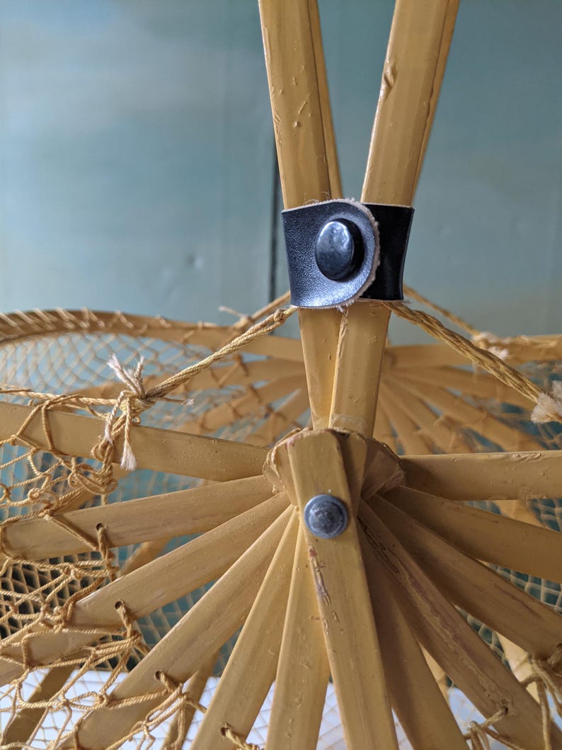 May include: Close-up of a vintage parasol's frame. The frame is made of light-colored wood, with a black leather strap and a metal button. The parasol's netting is visible, and the overall design is intricate and delicate.
