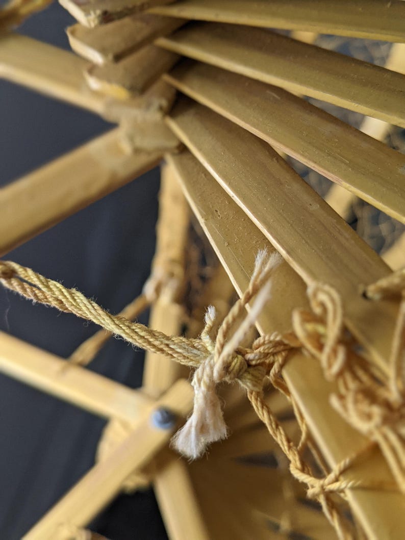 May include: Close-up of a bamboo structure with a woven design. The structure is held together with a twisted, light-brown rope. The bamboo is a light tan color, and the background is dark.