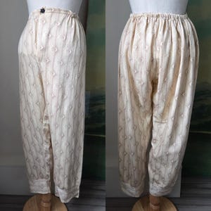 Peut inclure: Pantalon couleur crème avec un motif subtil de losanges et de rayures verticales. Le pantalon présente une taille élastique avec un bouton foncé au centre sur le devant et des ourlets à revers au bas de chaque jambe, vu de face et de dos.
