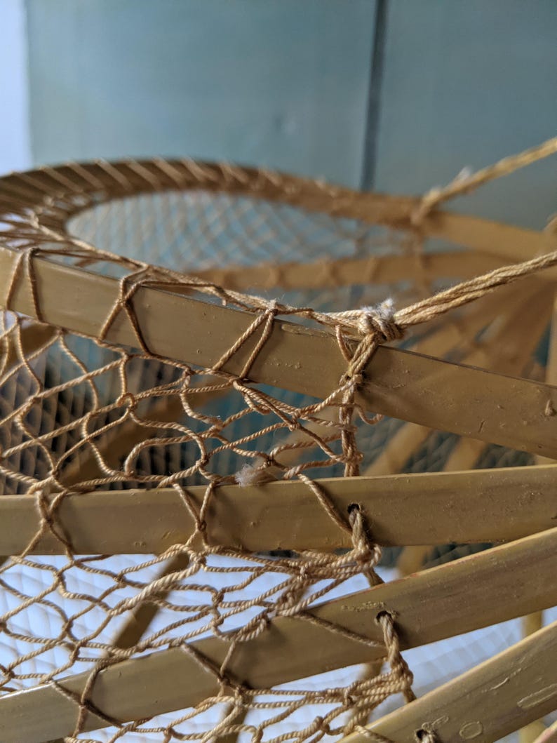 May include: Close-up of a vintage, handcrafted snowshoe. The frame is made of light brown wood, with a woven net of natural-colored twine. The twine is knotted to the frame, creating a sturdy and functional design. The snowshoe is a classic example of outdoor gear.