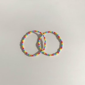 May include: Two rainbow beaded bracelets, one red, orange, yellow, green, blue, indigo, and violet, and the other violet, indigo, blue, green, yellow, orange, and red.