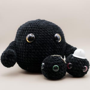 Könnte beinhalten: Drei schwarze gehäkelte Plüschtiere mit Glitz Augen. Das größte Spielzeug ist blob-förmig mit zwei kleinen Armen. Die beiden kleineren Spielzeuge sind rund und haben Schlüsselanhänger.