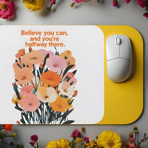 以下が含まれることがあります： 黄色と白のフラワーデザインのマウスパッドで、"Believe you can, and you're halfway there."というテキストが書かれています
