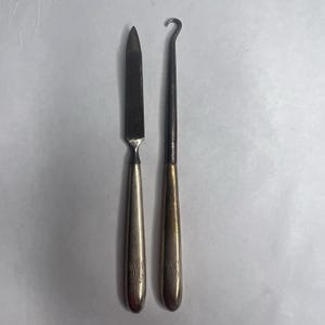 May include: Two vintage metal tools. One is a small knife with a silver handle and a dark blade. The other is a crochet hook with a gold handle and a curved hook end. Both handles have engraved initials.