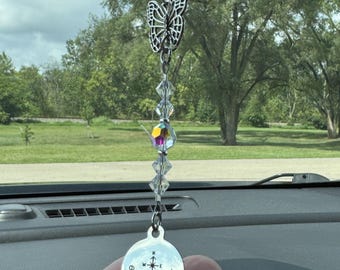 May include: A car charm featuring a silver butterfly pendant, clear crystal beads, and iridescent accents. The charm includes a round pendant with a compass design and the words "enjoy the journey."