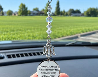 May include: A silver-toned car rearview mirror charm featuring a metal angel pendant and a round disc engraved with the text: Guardian Angel Please protect me, my passengers and all who pass by. The charm includes clear faceted crystal beads.