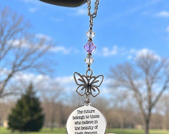 May include: A silver-toned hanging ornament featuring a circular metal charm engraved with the text, The future belongs to those who believe in the beauty of their dreams. Eleanor Roosevelt. It includes a butterfly charm and two clear beads.