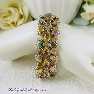 May include: A beaded bracelet featuring iridescent, multi-colored square beads and clear, textured round beads with red and gold flecks, woven together with small gold-toned seed beads. The text IndulgedGirl@etsy.com is printed in purple.