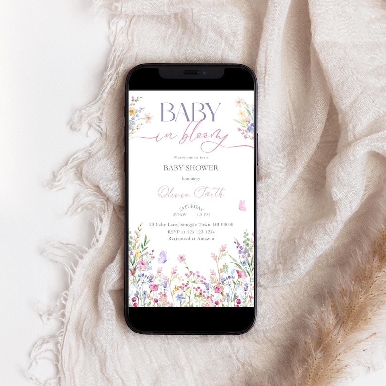 May include: A smartphone displays a baby shower invitation. The invitation features the text "BABY in bloom" in a script font, along with floral and butterfly illustrations. The invitation includes details such as the date, time, location, and RSVP information.