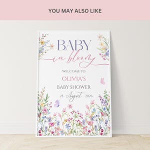 May include: A framed baby shower sign with floral watercolor illustrations. The sign reads "BABY in bloom" and welcomes guests to Olivia's baby shower on August 25, 2026. The design features pastel colors and butterflies.