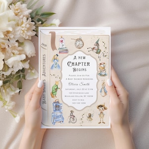 May include: A baby shower invitation with a storybook theme. The invitation features illustrations of classic storybook characters and the text "A New Chapter Begins". The invitation is held by a person.