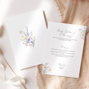 May include: Two white baby shower announcement cards. One card features a watercolor floral bouquet in pastel colors. The other card has text that reads "Baby [Name] is on the way!" and "Thank you" with additional text.