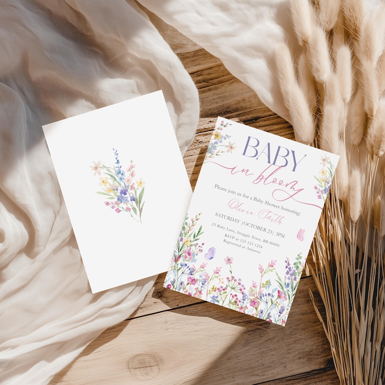 May include: Two white cards with floral designs. One card features a watercolor bouquet, the other reads "BABY in bloom" with event details. The invitation is for a baby shower honoring Olivia Faith.