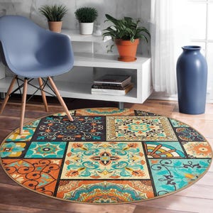 Könnte beinhalten: Ein runder Teppich mit Patchwork-Design. Der Teppich zeigt quadratische Muster in Türkis, Orange, Gelb und Braun. Er liegt auf einem Holzboden, mit einem blauen Stuhl und einem weißen Regal im Hintergrund. Durchmesser: ca. 150 cm.