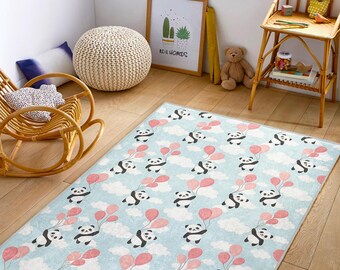 May include: A rectangular area rug with a light blue background featuring a pattern of pandas holding pink balloons, set against white clouds. The rug is placed on a wooden floor.