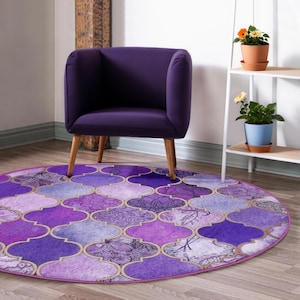 May include: A round area rug with a Moroccan tile pattern in shades of purple, lavender, and gold. A purple armchair with wooden legs sits above the rug. The rug's design includes floral and geometric elements, creating a decorative floor covering.