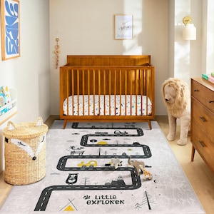 Könnte beinhalten: Ein Kinderzimmer mit einem Holzbett, einem Teppich mit Straßenmotiv mit Spielzeugautos und -tieren sowie einem Weidenkorb. Der Teppich hat einen grauen Hintergrund mit einem schwarzen Straßendesign und dem Text "Little Explorer".