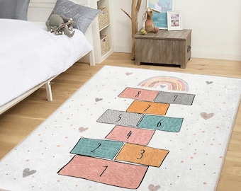 May include: A rectangular hopscotch rug with a white background, featuring colorful hopscotch squares numbered 1 through 9. A rainbow and hearts decorate the top. The rug is in a child's bedroom.