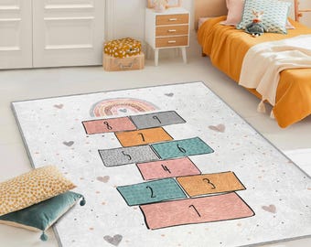 Puede incluir: Una alfombra de juego blanca y gris con un arcoíris y un juego de la rayuela impreso en ella. El juego de la rayuela tiene los números del 1 al 9 y está en formación apilada. La alfombra tiene un fondo blanco con lunares grises y rosas.