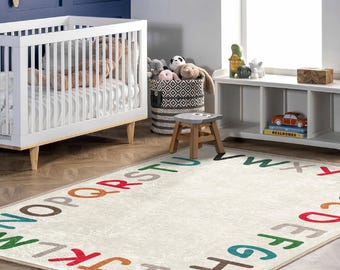 May include: A white crib with a white and gray striped mattress, a white storage bench with three shelves, a white and black woven basket filled with stuffed animals, and a white alphabet rug with colorful letters.