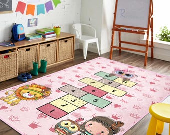 May include: A pink children's rug featuring a hopscotch grid with numbers and cartoon characters like a lion, owl, and a girl. The rug is decorated with crowns, hearts, and the word "love".