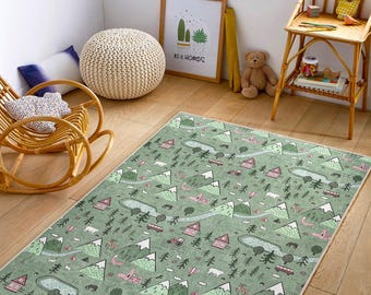 Op de afbeelding: Een rechthoekig groen tapijt met een berg- en bosontwerp. Het tapijt heeft illustraties van bergen, bomen, huizen, voertuigen en dieren in roze, grijs en wit. Het tapijt ligt op een houten vloer.