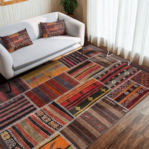 Può includere: Un tappeto patchwork colorato con una varietà di motivi geometrici in tonalità di rosso, arancione, marrone e nero. Il tappeto è steso su un pavimento in legno duro in un soggiorno.