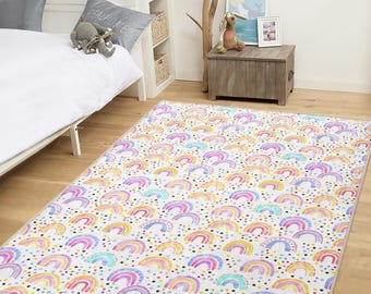 May include: A rectangular area rug with a repeating pattern of watercolor rainbows in pastel colors. The rainbows are in shades of pink, yellow, blue, and purple, with small, colorful polka dots scattered across a white background. The rug is placed on a wooden floor.