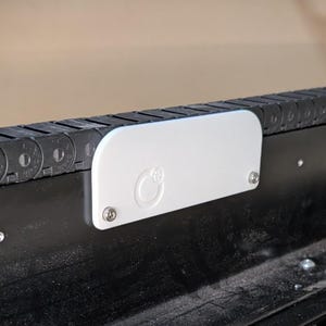 May include: A white plastic cover with a circular logo on a black cable chain system.