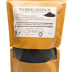 May include: A brown paper bag with a clear window, filled with dark soil. The bag features a white label with the text "WORM CASTINGS" and details about its benefits as an organic soil amendment and fertilizer. The bag contains 1 quart of product.
