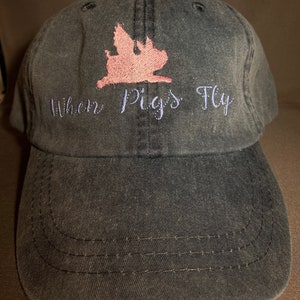 Puede incluir: Una gorra de béisbol negra con una silueta de cerdo rosa y el texto "Where Pigs Fly" bordado en la parte delantera.