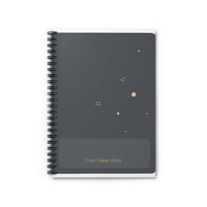 Peut inclure: Un carnet à spirales gris foncé orné d'un motif de petites formes géométriques et de points dorés sur la couverture. Une section rectangulaire en bas contient le texte Your Name Here en lettres dorées, offrant un espace de personnalisation.
